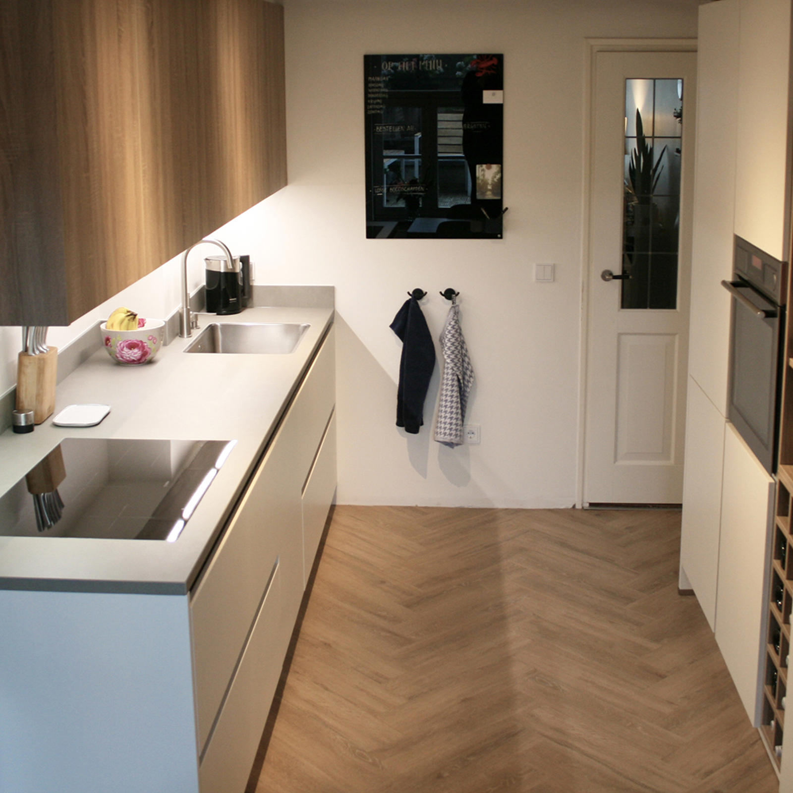 Maatwerk keuken in Maastricht: lange keukenwand met grijs werkblad tegenover hoge kast met oven en wijnrek