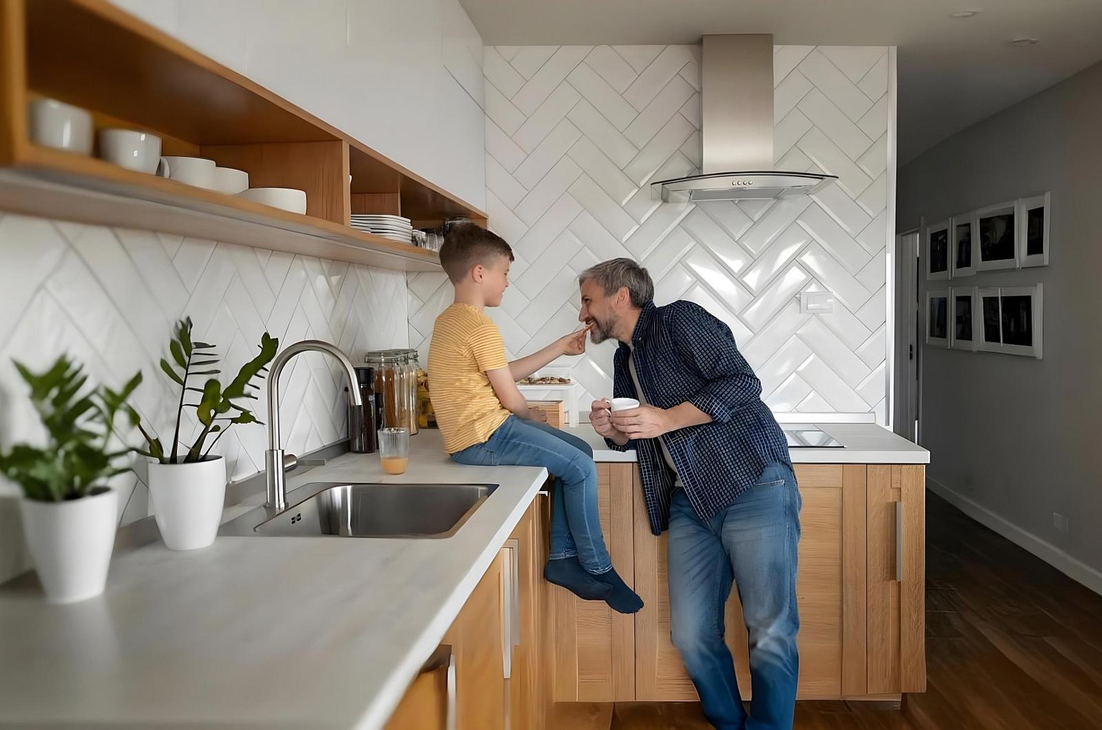 Vader en zoon op het werkblad van een keuken met witte visgraattegels en open houten schappen