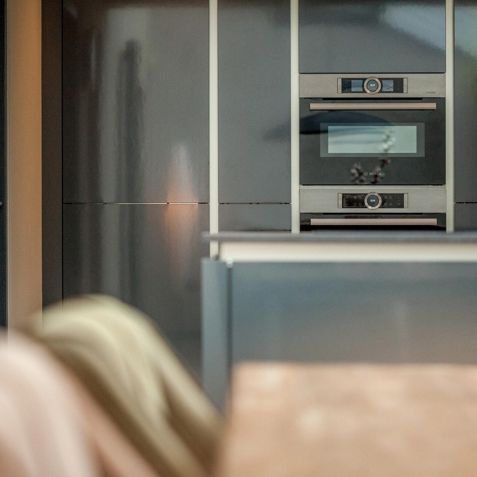 Twee inbouwovens in hoge grijze kastenwand gezien vanaf de eettafel