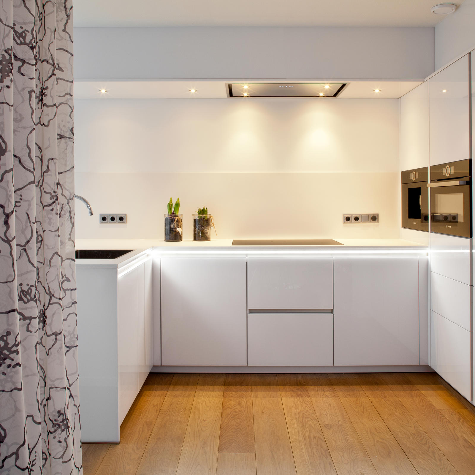 Designkeuken in Maastricht: witte greeploze keuken met hoge kastenwand, twee inbouwovens en houten vloer