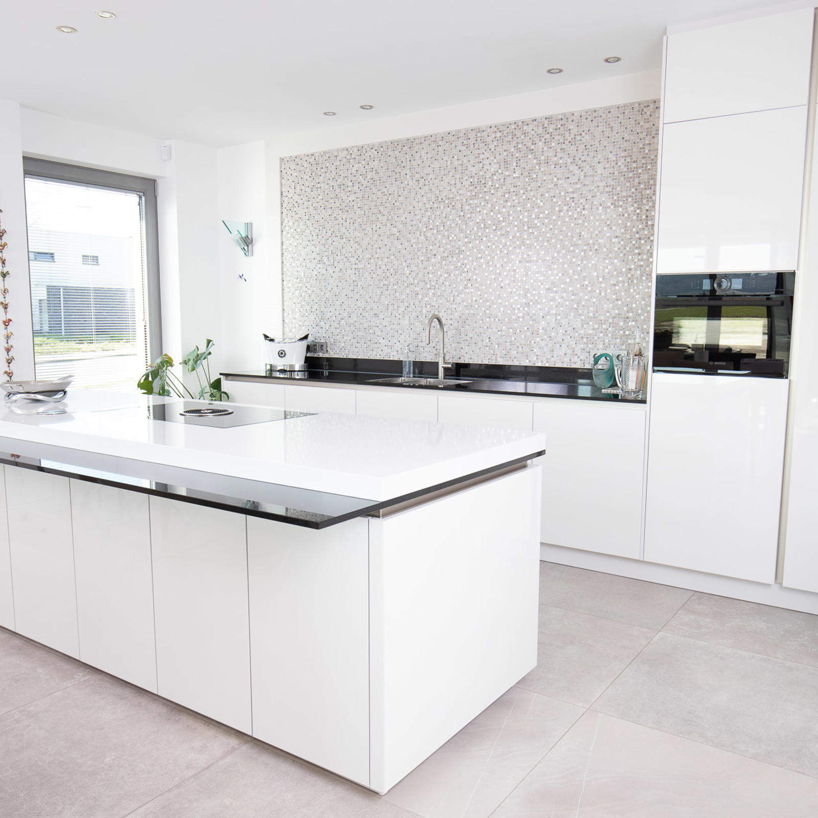 Moderne witte keuken in Maastricht: wit hoogglans kookeiland, mozaïeken achterwand en hoge kastenwand met oven