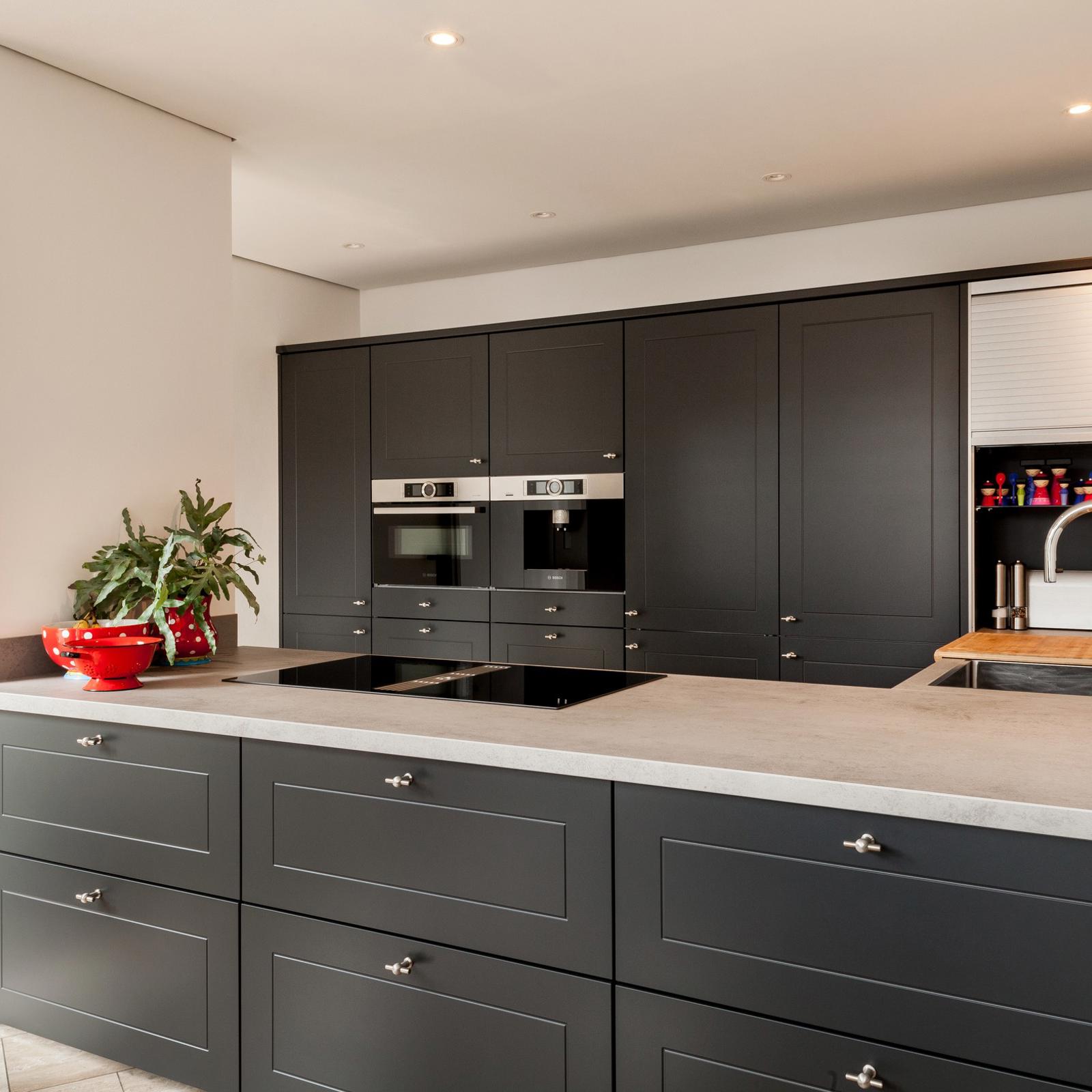 Antraciet keuken in Nuth: antraciet kaderfronten met betonlook werkblad, inductiekookplaat en hoge kastenwand met inbouwapparatuur