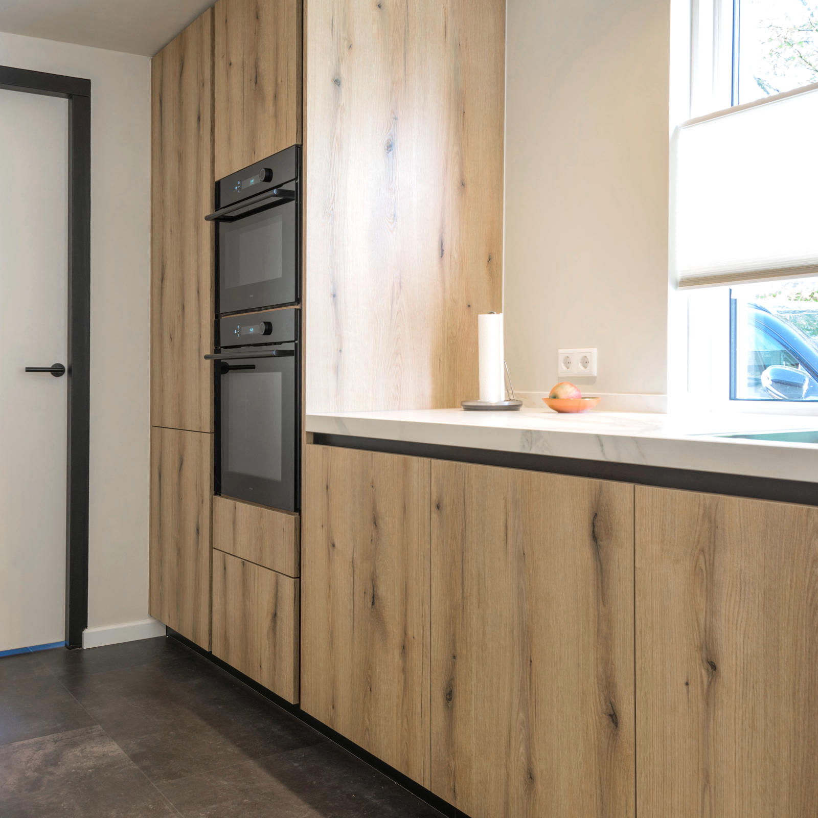 Hoge kast in eikenlook met twee zwarte inbouwovens naast het raam