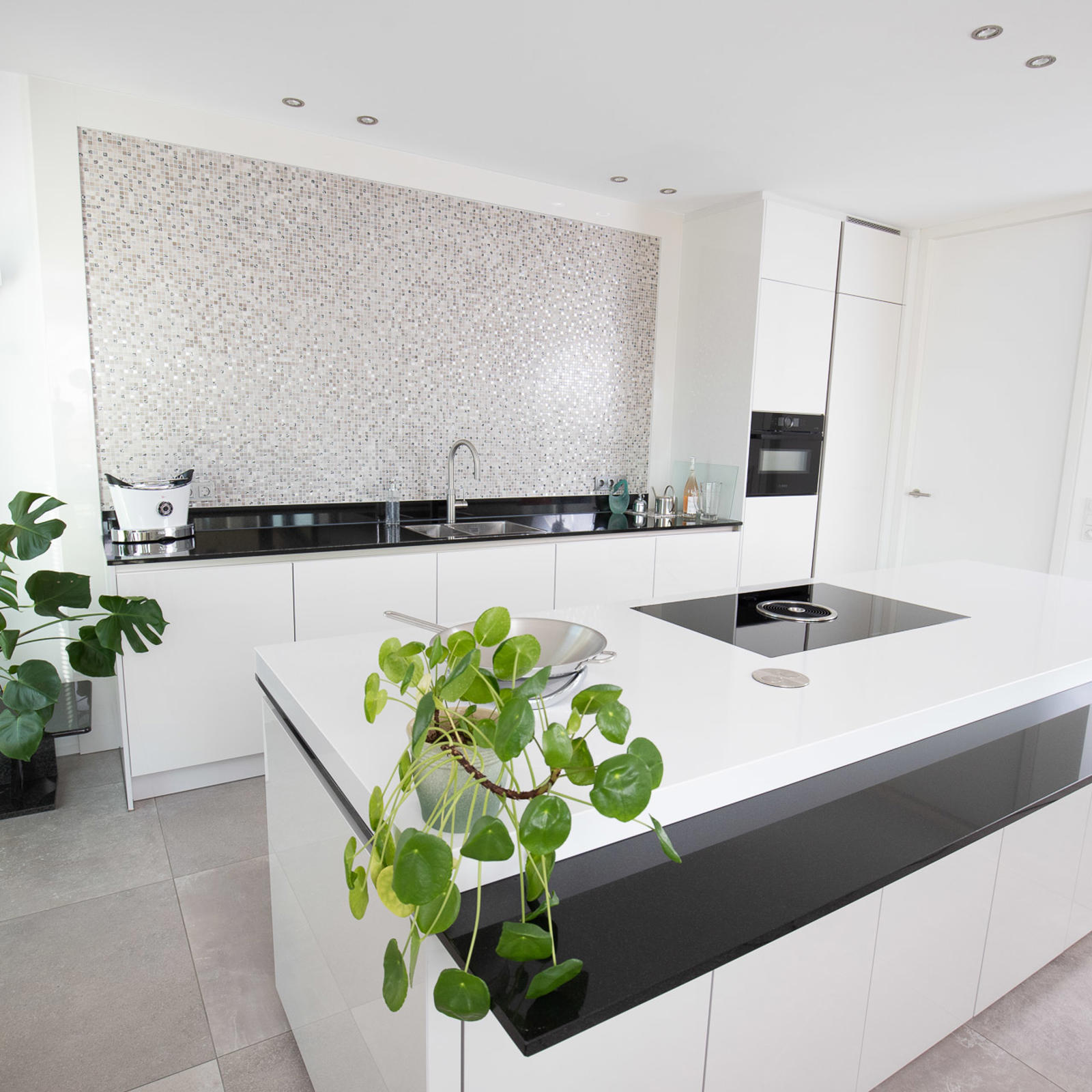 Moderne witte keuken in Maastricht: wit kookeiland met dubbel werkblad, mozaïeken achterwand en zwart aanrechtblad