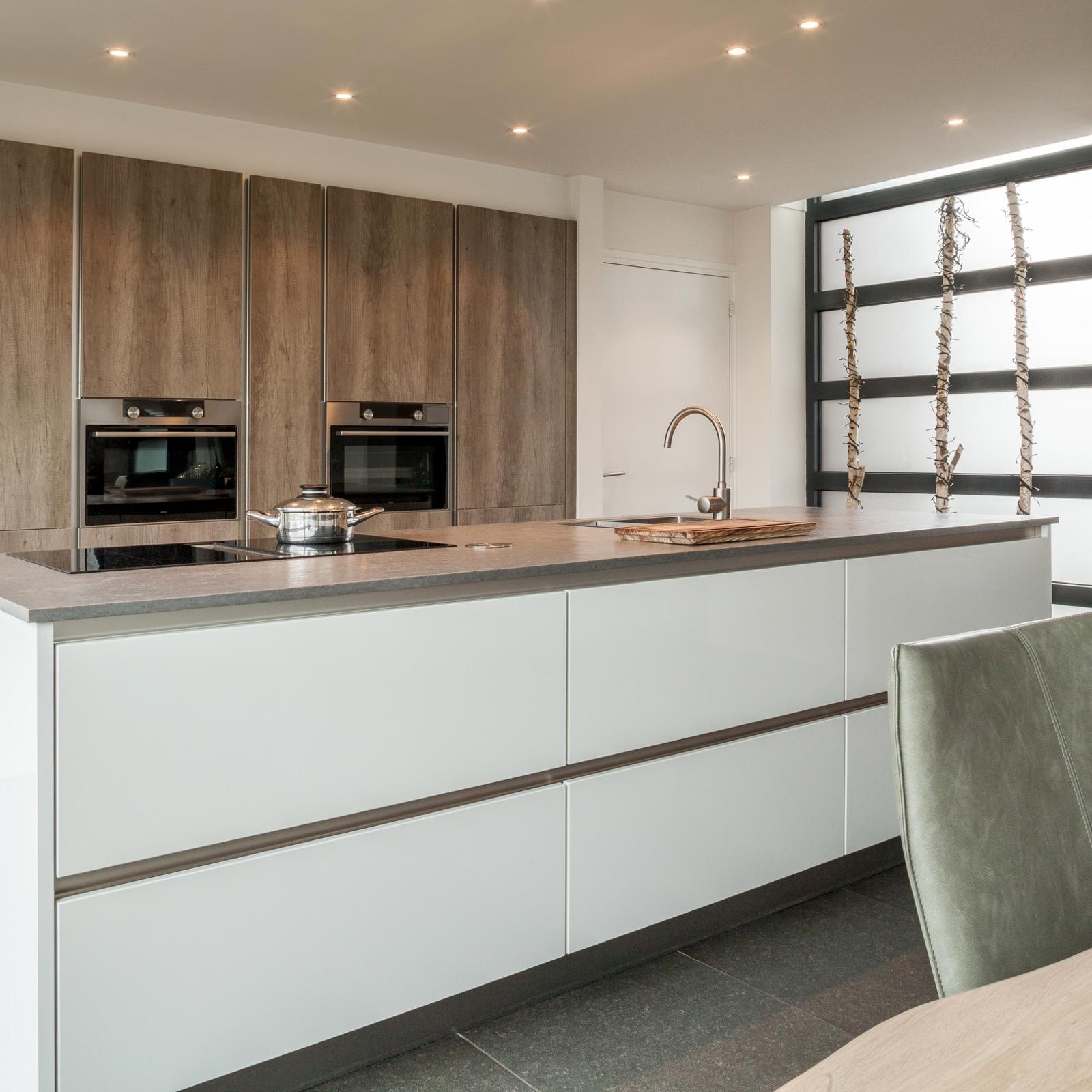 Houtlook keuken in Brunssum: wit kookeiland met inductiekookplaat en greeplijsten voor een houtlook kastenwand