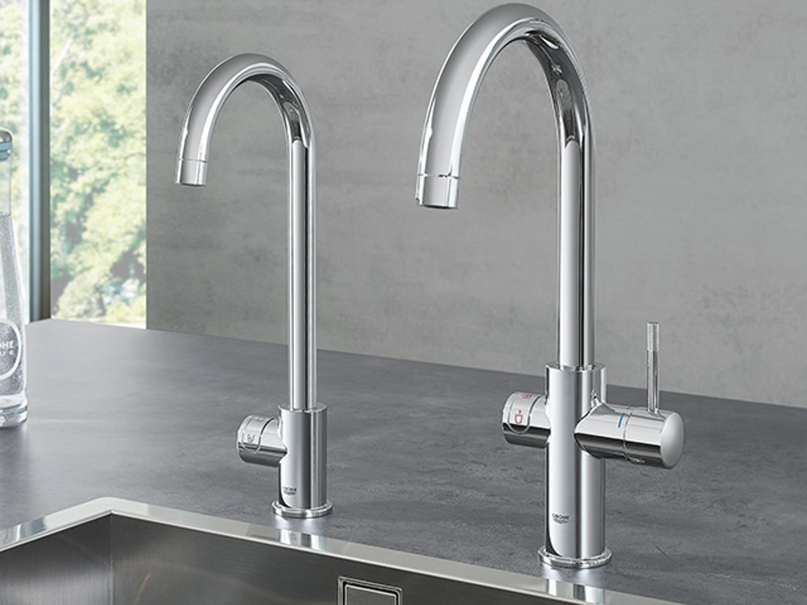 GROHE chromen kranen naast elkaar boven een rvs spoelbak in een grijs werkblad
