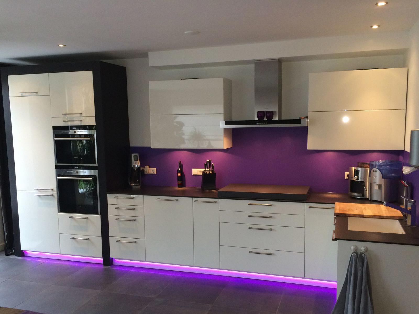 Bokmerk achterwand in paars achter een witte hoogglans keuken met paarse plintverlichting