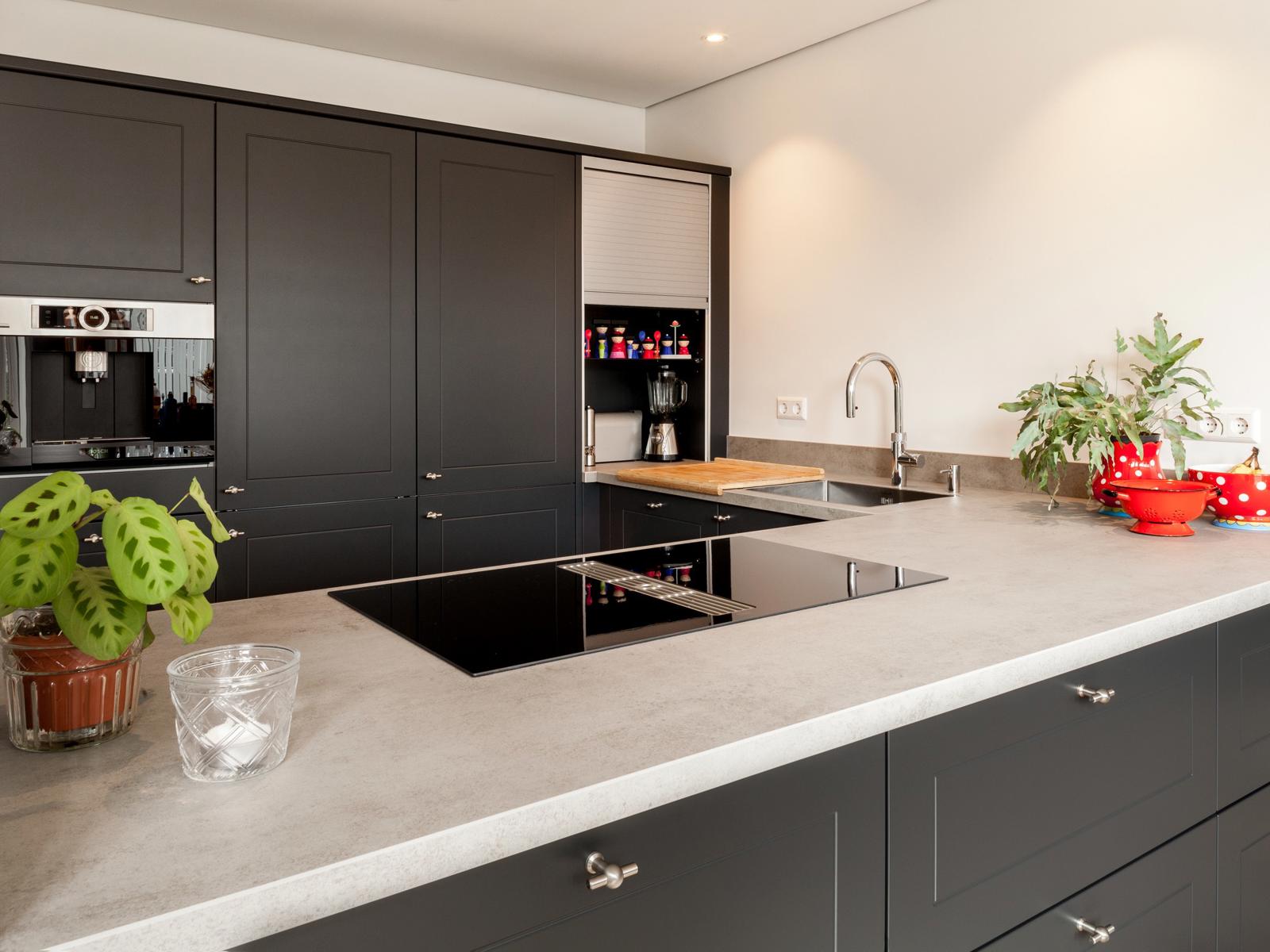 Antraciet keuken in Nuth: hoekopstelling met betonlook werkblad, inductiekookplaat, spoelbak en hoge kasten met oven