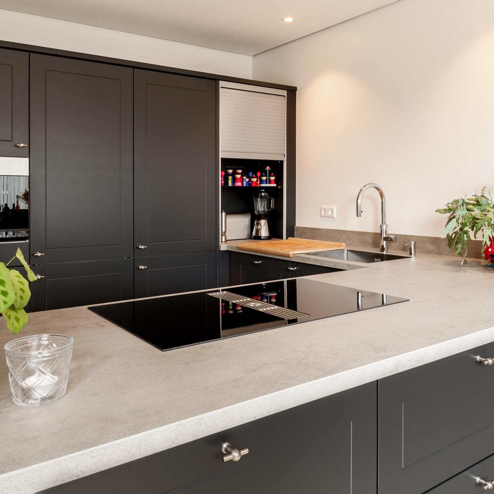 Antraciet keuken in Nuth: hoekopstelling met betonlook werkblad, inductiekookplaat, spoelbak en hoge kasten met oven
