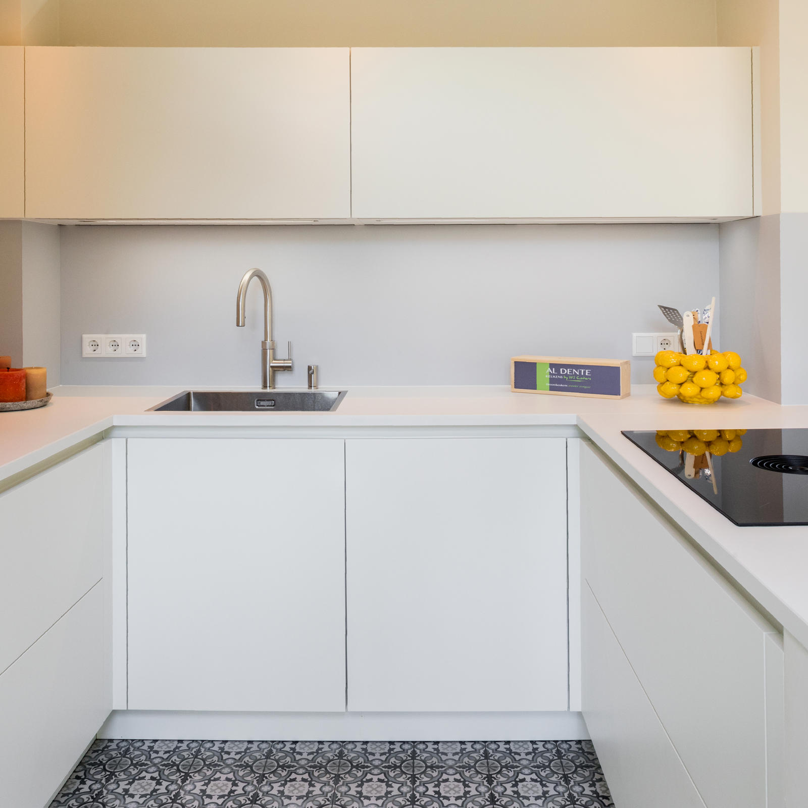 Witte U-vormige keuken met RVS spoelbak, greeploze kasten en patroontegels op de vloer