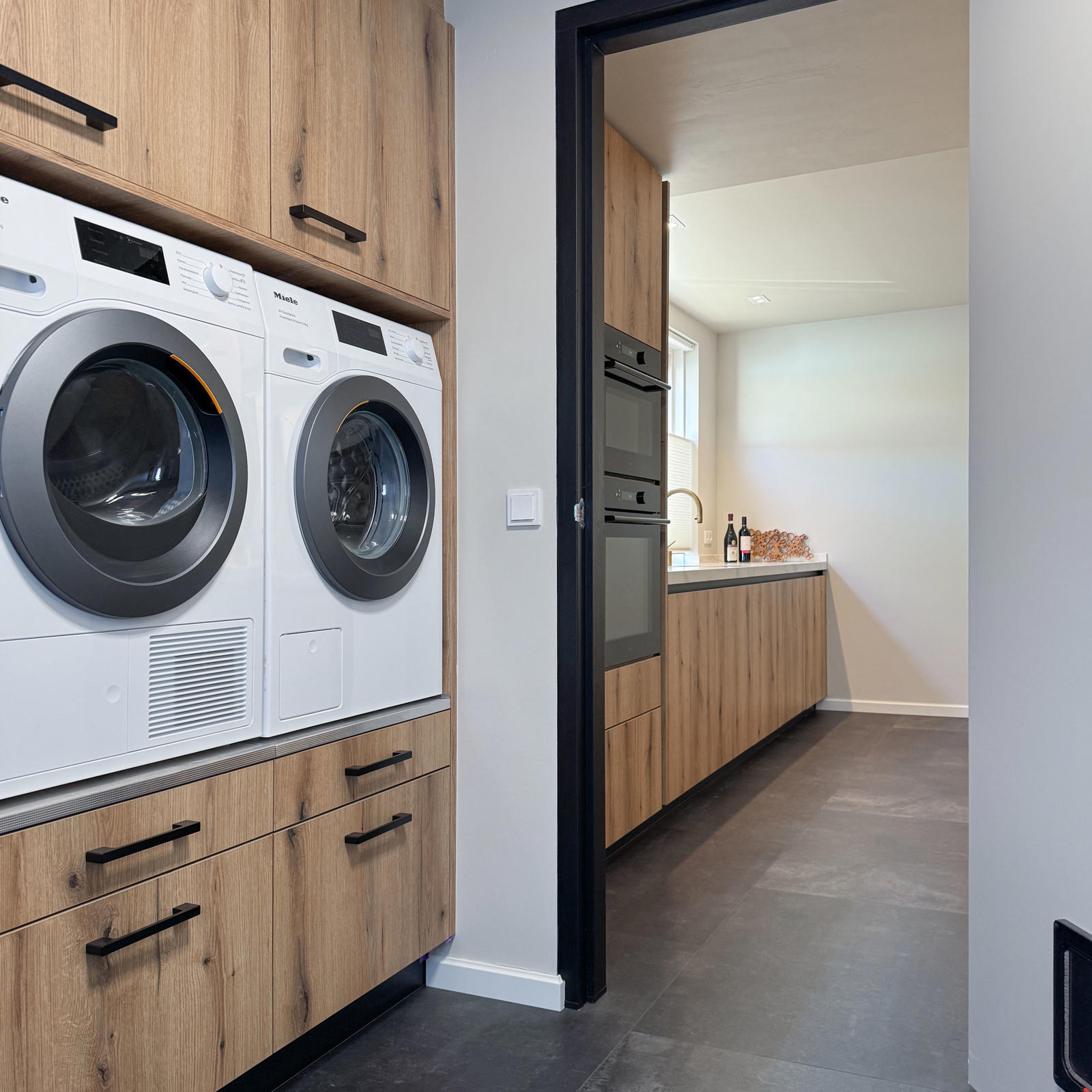 Doorkijk vanuit de bijkeuken met wasmachine en droger naar de keuken in eikenlook